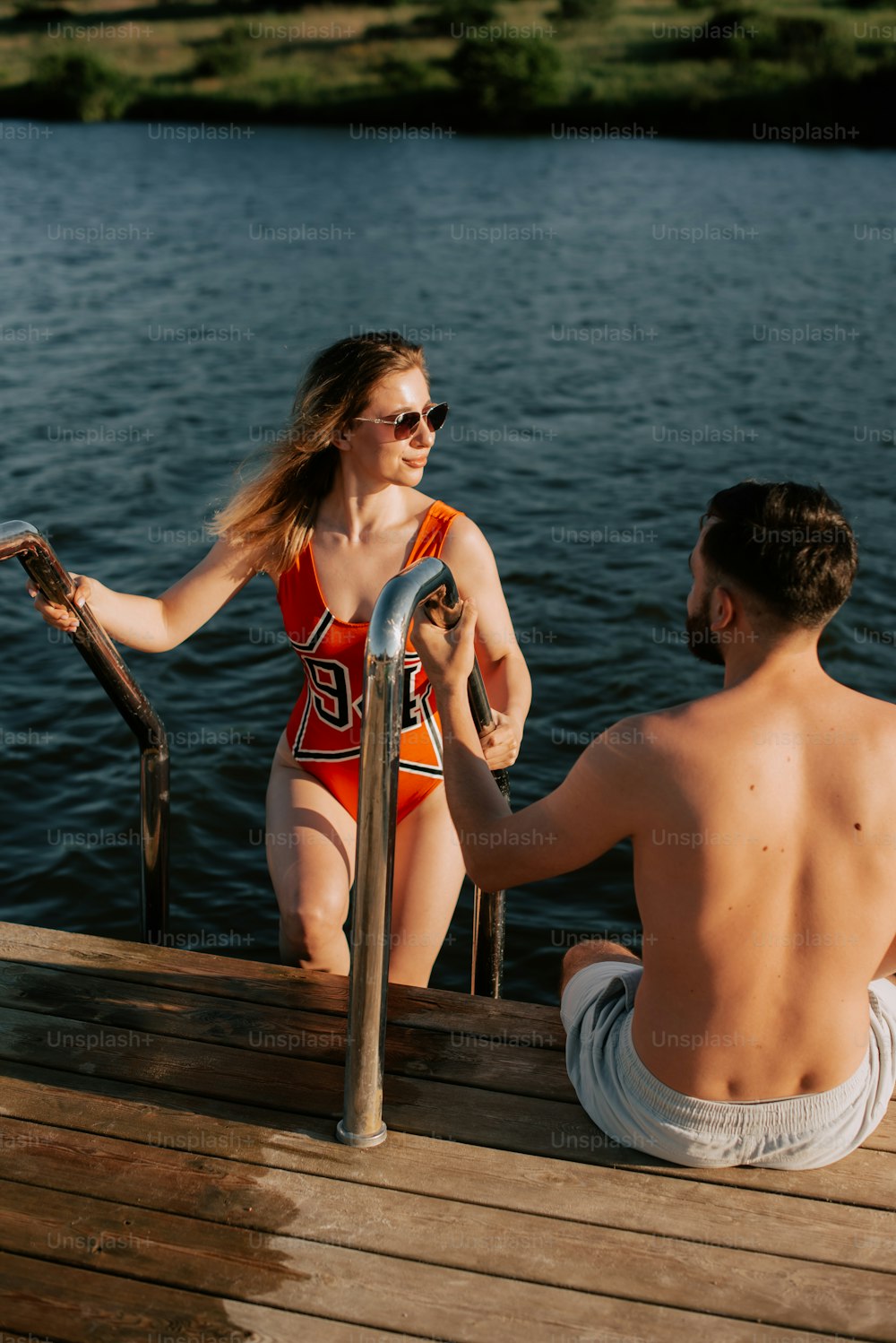 a man and a woman sitting on a dock next to a body of water