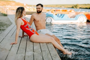 a man and a woman sitting on a dock next to a body of water