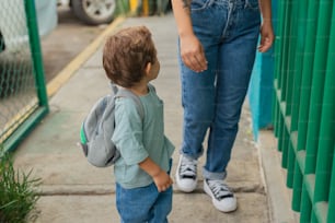 a little boy standing next to a woman on a sidewalk