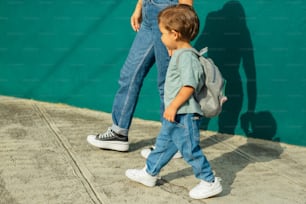 a little boy walking down a sidewalk next to a woman