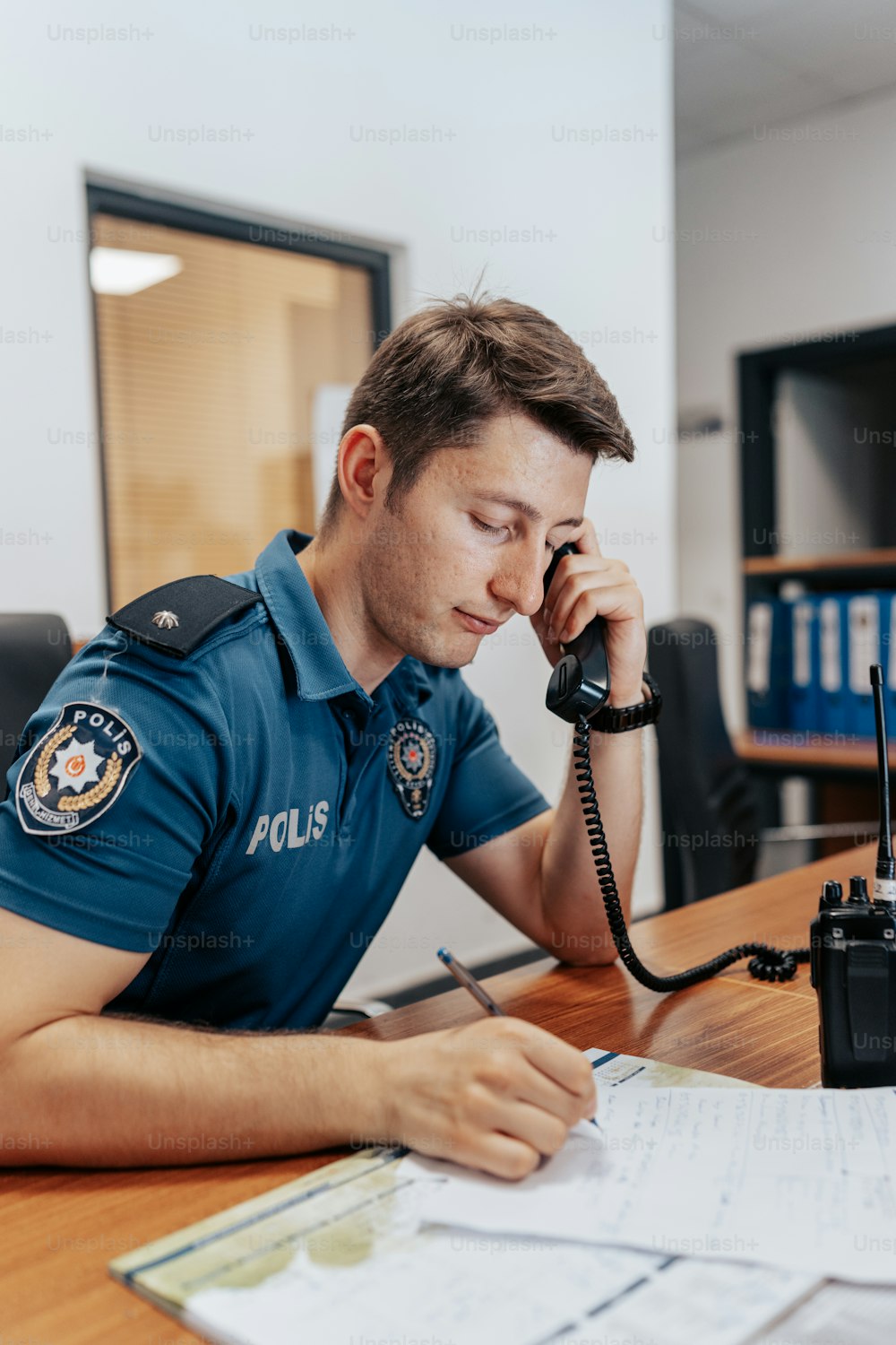 a police officer sitting at a desk talking on a phone