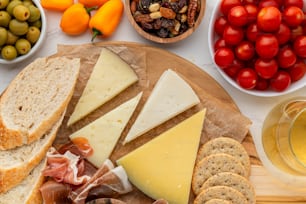 uma variedade de queijos, bolachas, azeitonas, tomates e pão