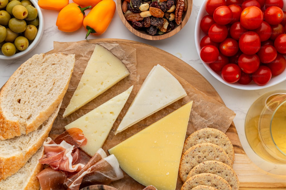 a variety of cheeses, crackers, olives, tomatoes, and bread