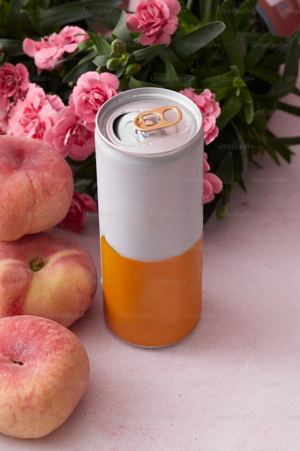 a can of peach soda next to pink flowers