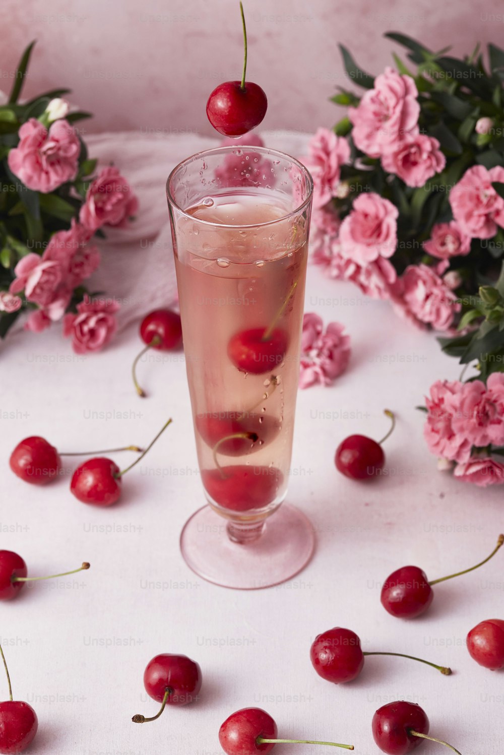 a glass filled with liquid and cherries on a table