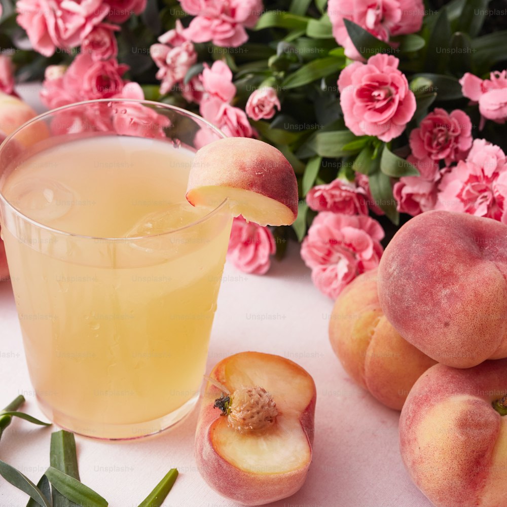 ein Glas gefüllt mit einem Getränk neben rosa Blumen