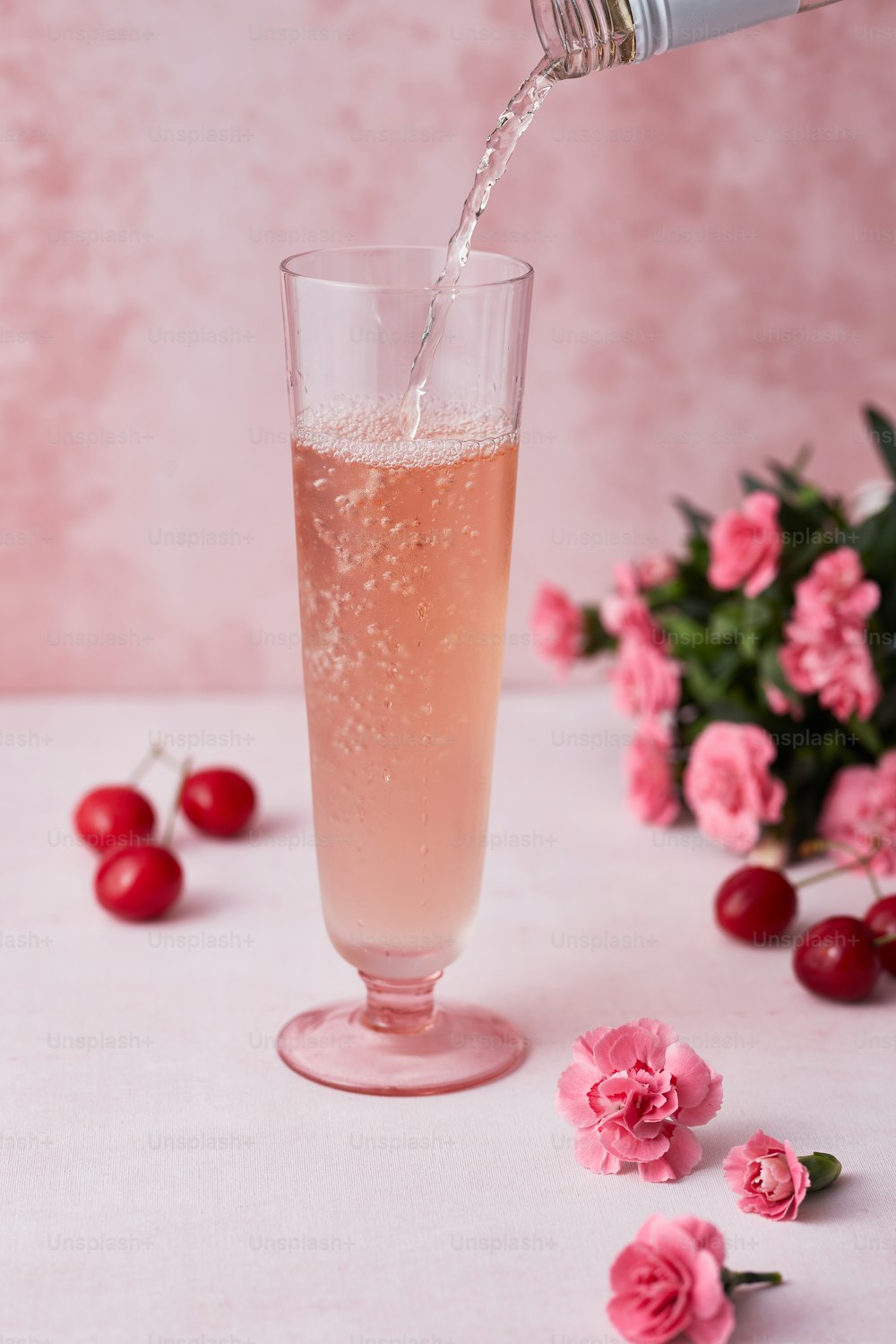 a glass filled with liquid next to pink flowers
