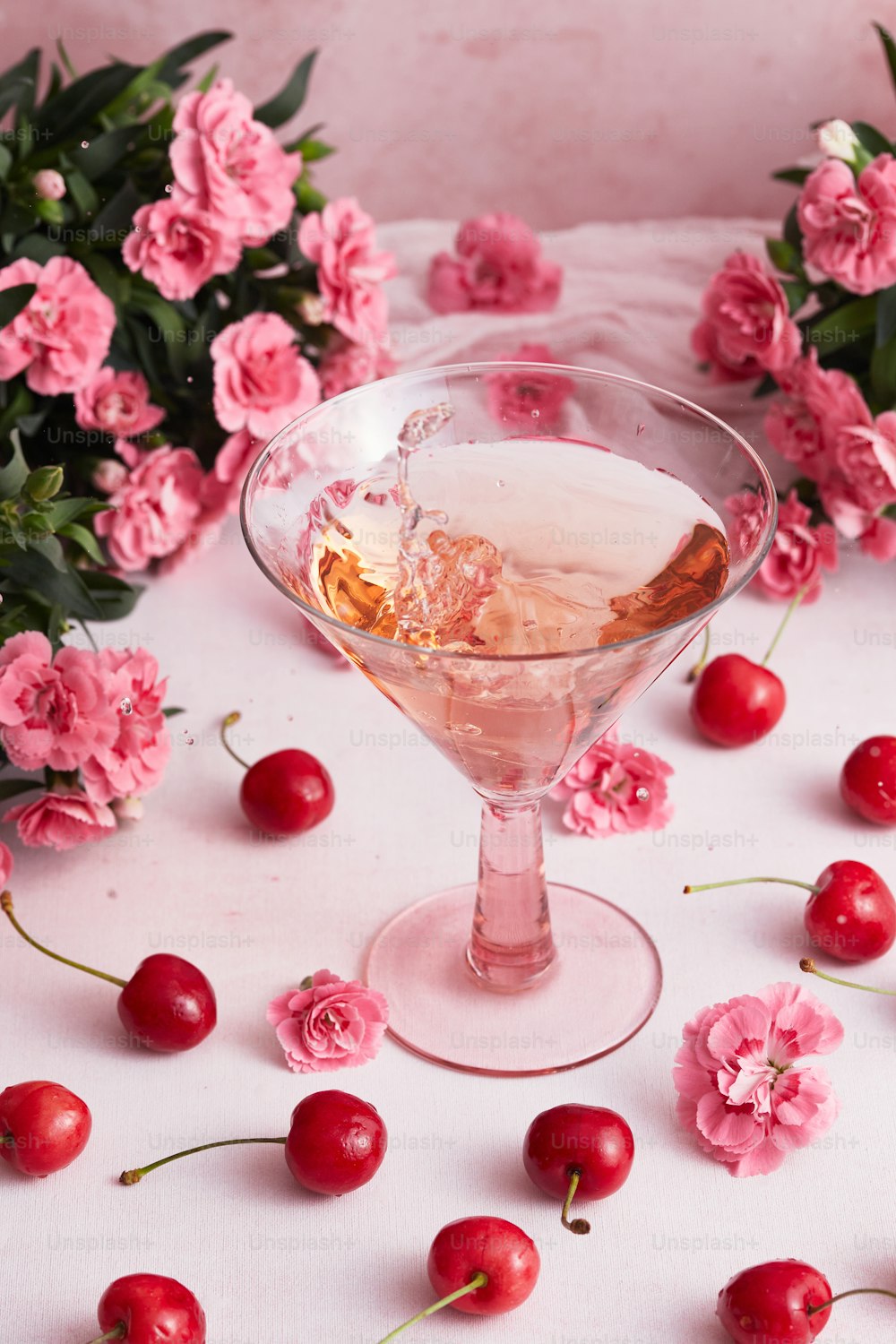 a glass filled with a liquid surrounded by flowers and cherries