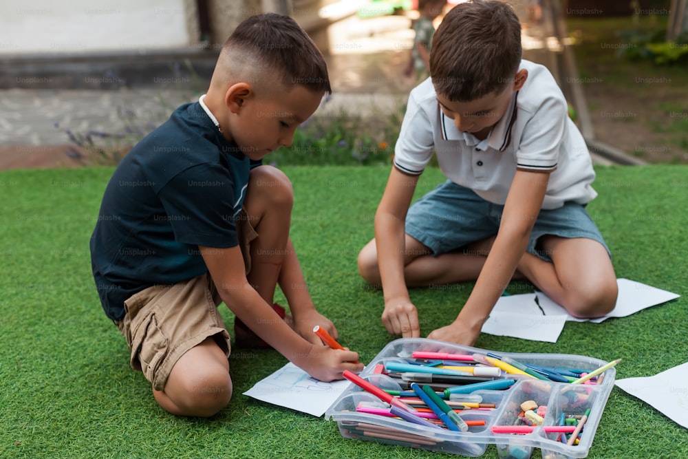 two young boys sitting on the grass playing with pencils