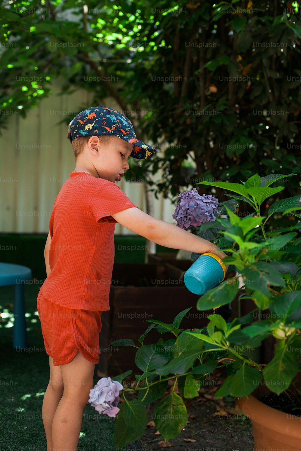 a young boy in a red shirt is watering flowers
