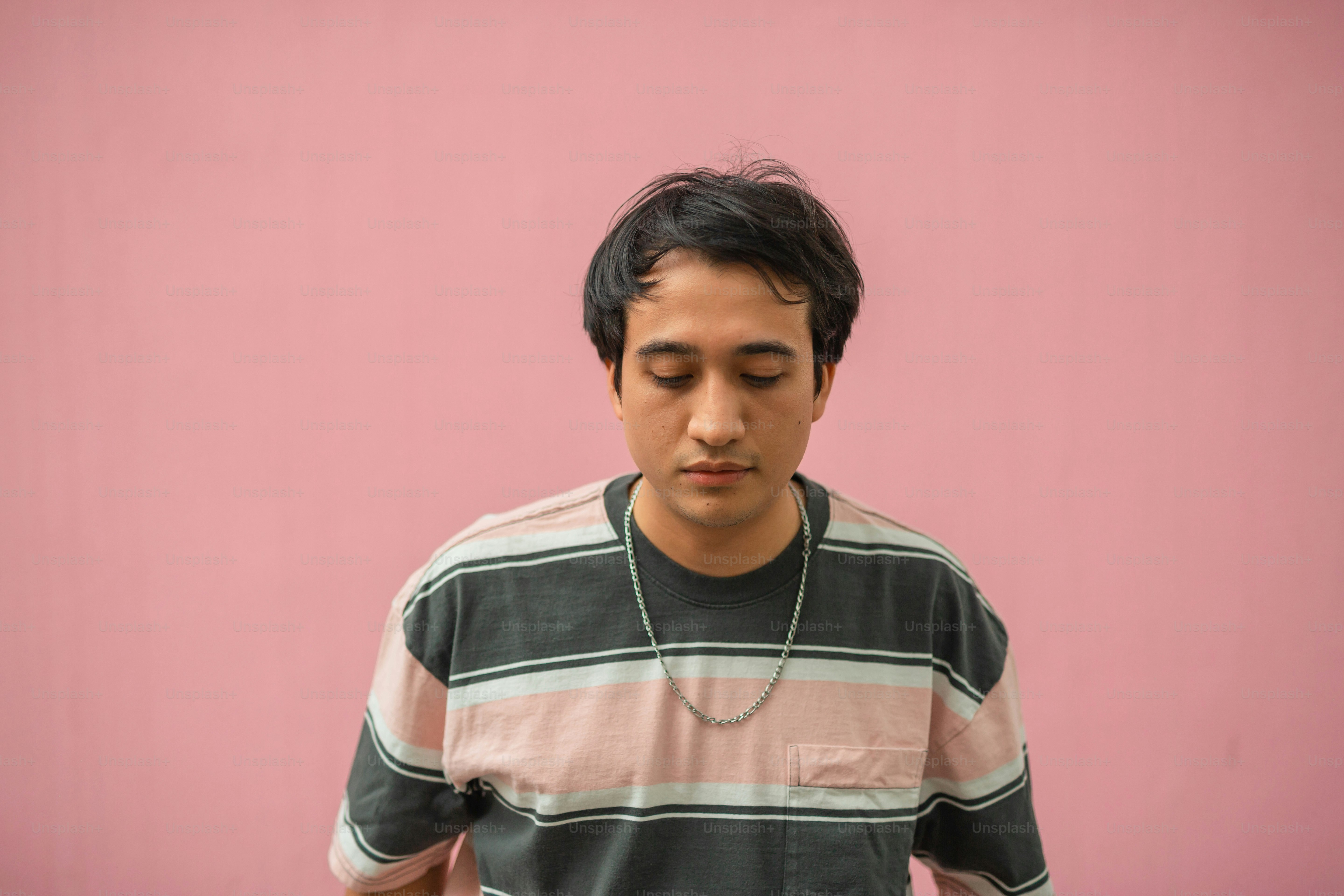 a man with a necklace on his neck standing in front of a pink wall
