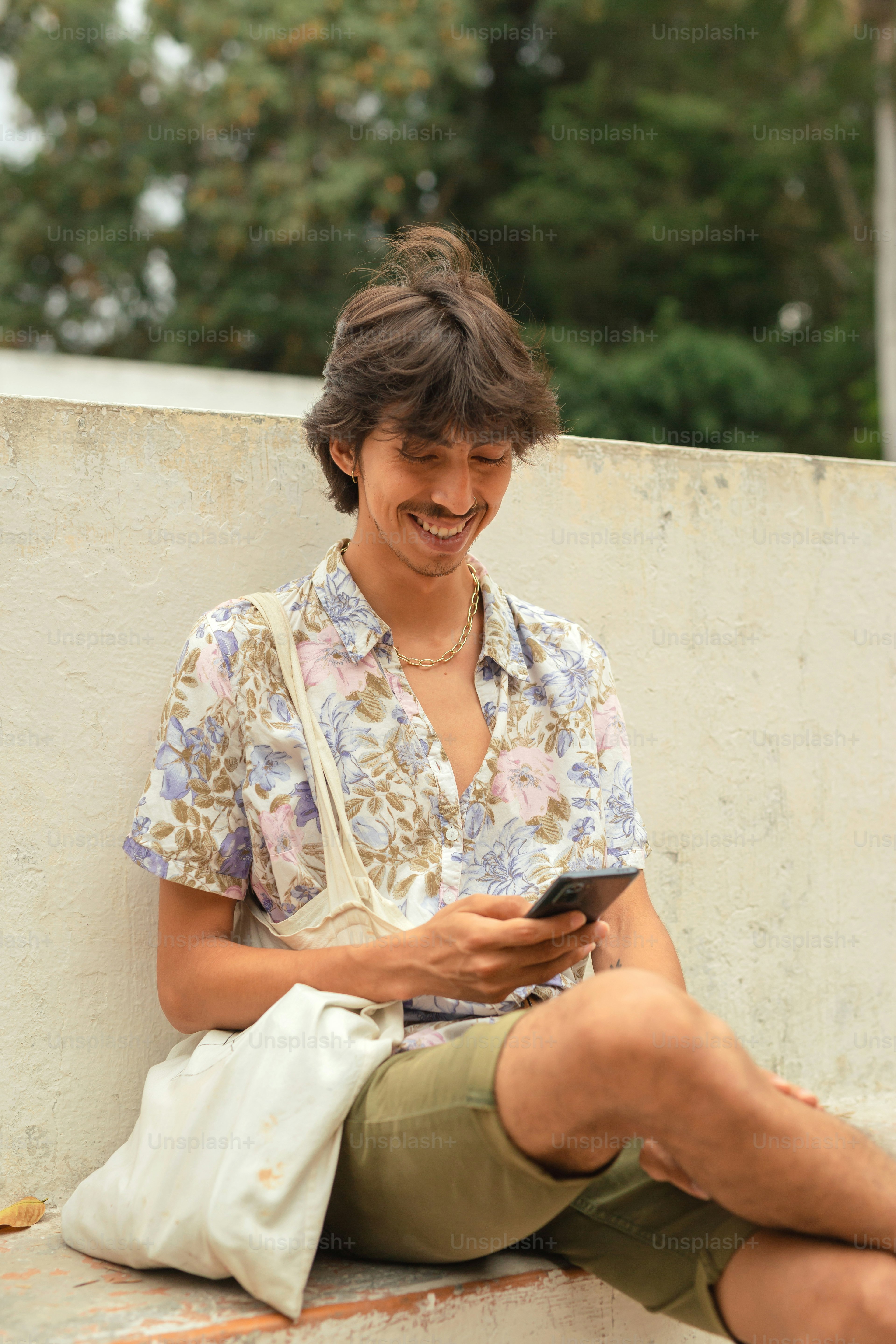 A man sitting on a ledge looking at his cell phone photo – Smiling ...