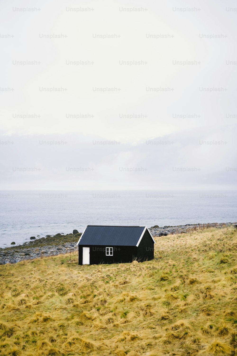 uma pequena casa preta sentada em cima de um campo coberto de grama