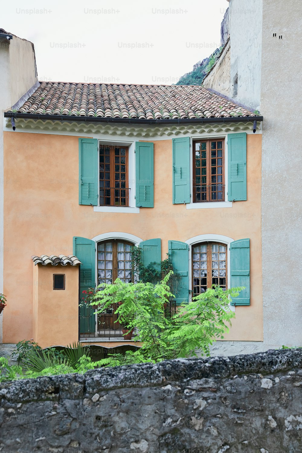 una casa con persiane verdi e un muro di pietra