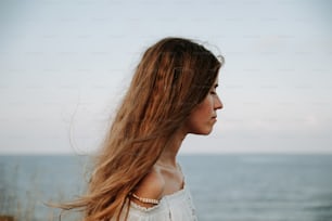 a woman with long hair standing in front of the ocean