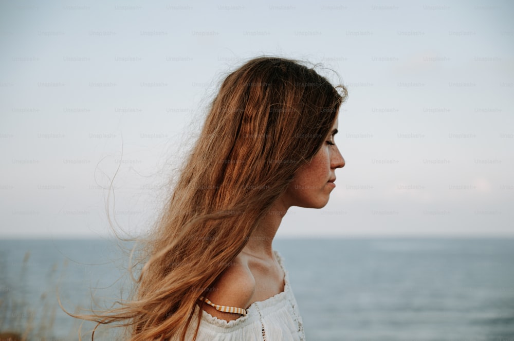 a woman with long hair standing in front of the ocean