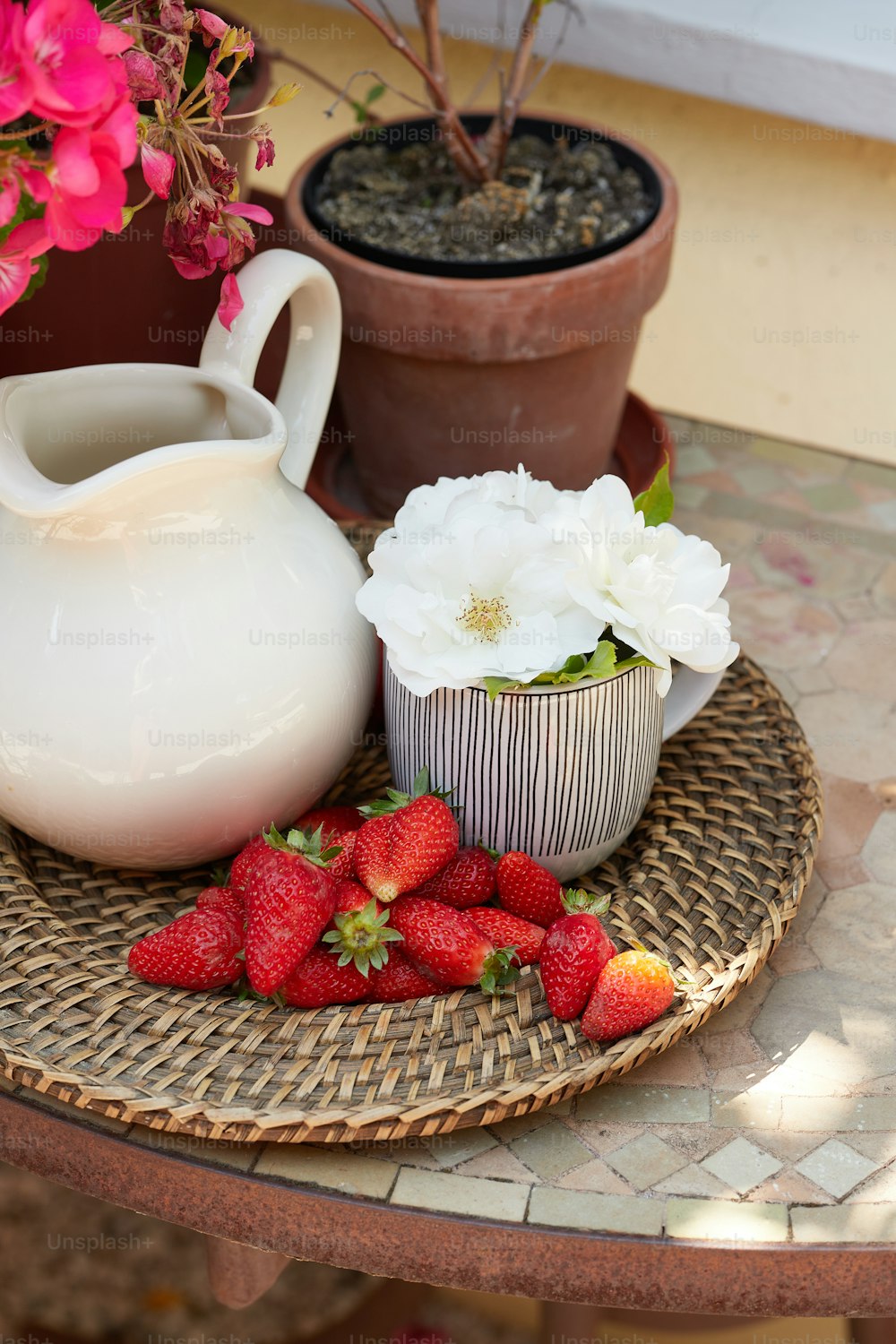 un plato de fresas y una jarra de flores sobre una mesa