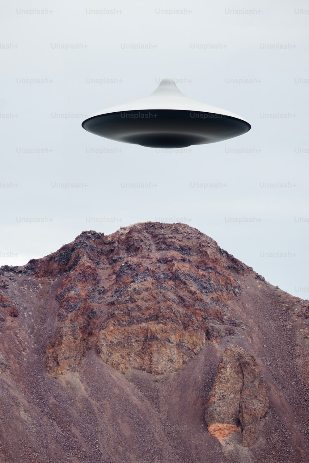 a large black object flying over a mountain
