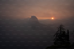 the sun is setting over the mountains in the fog