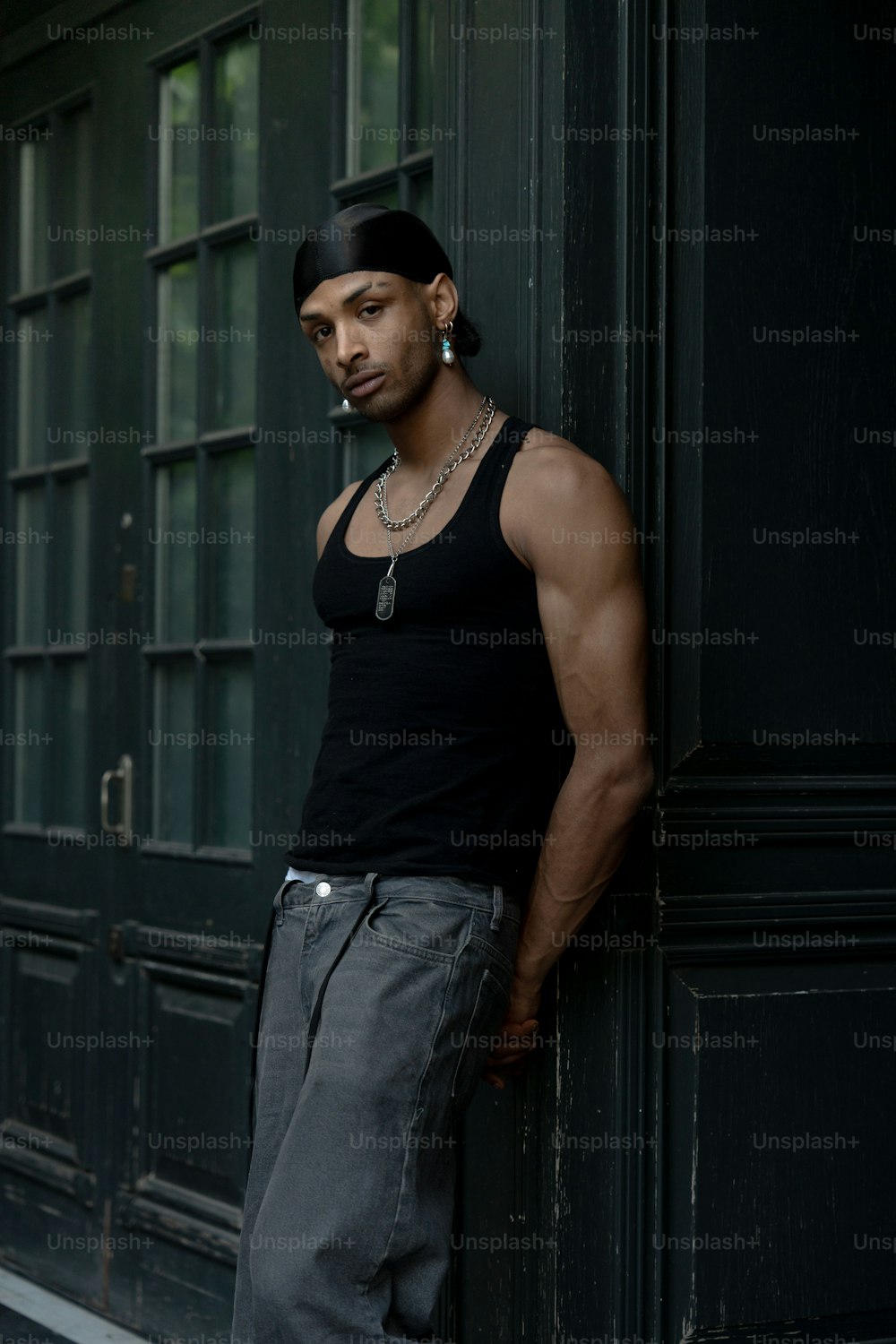 a man leaning against a wall wearing a black tank top