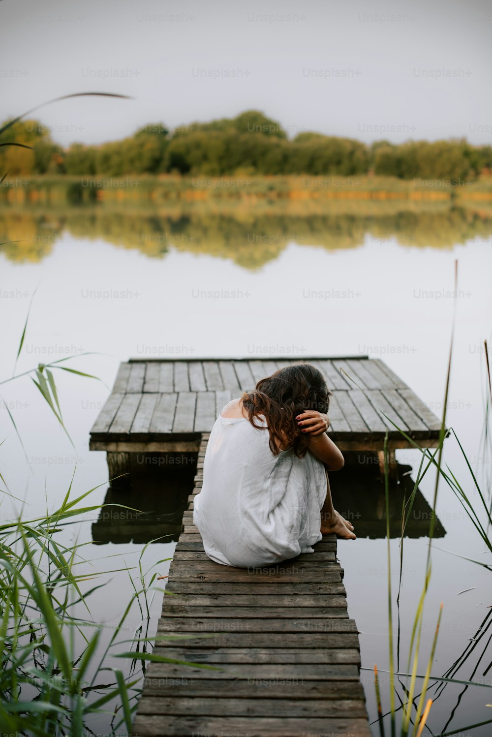 Una donna seduta su un molo accanto a uno specchio d'acqua