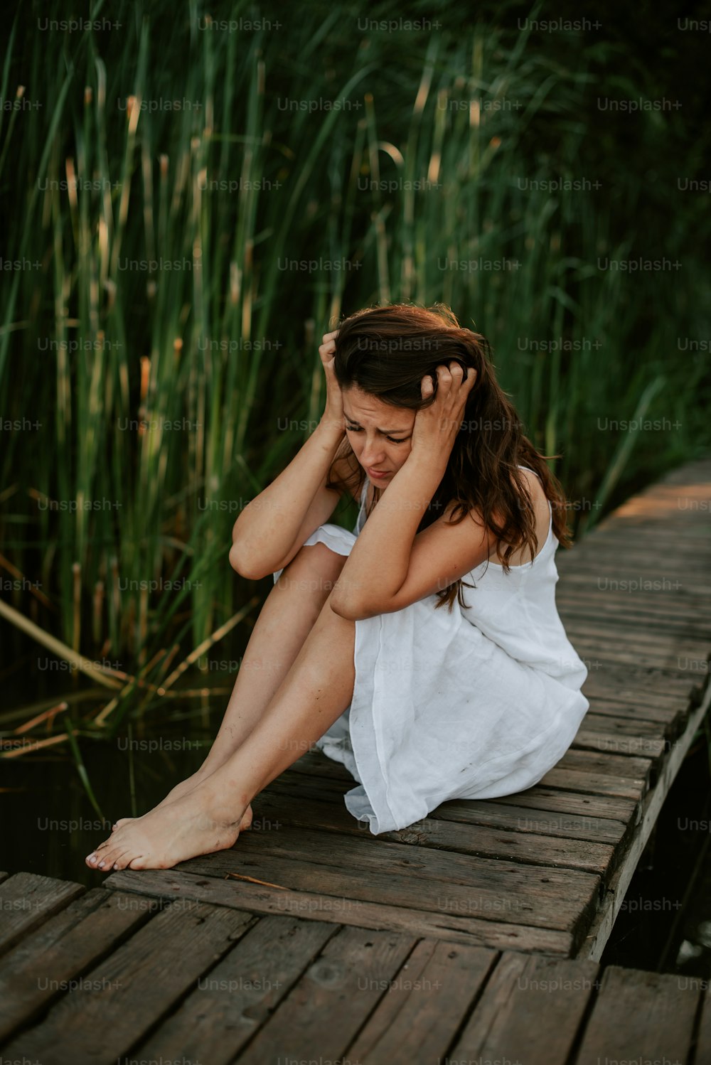 a woman sitting on a dock with her head in her hands