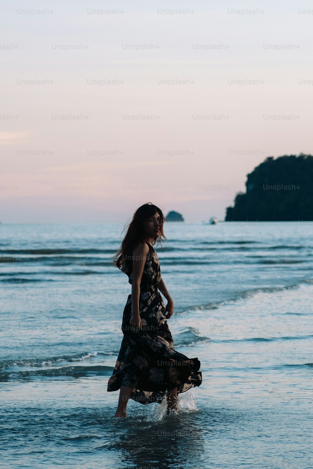 a woman in a long dress walking into the ocean