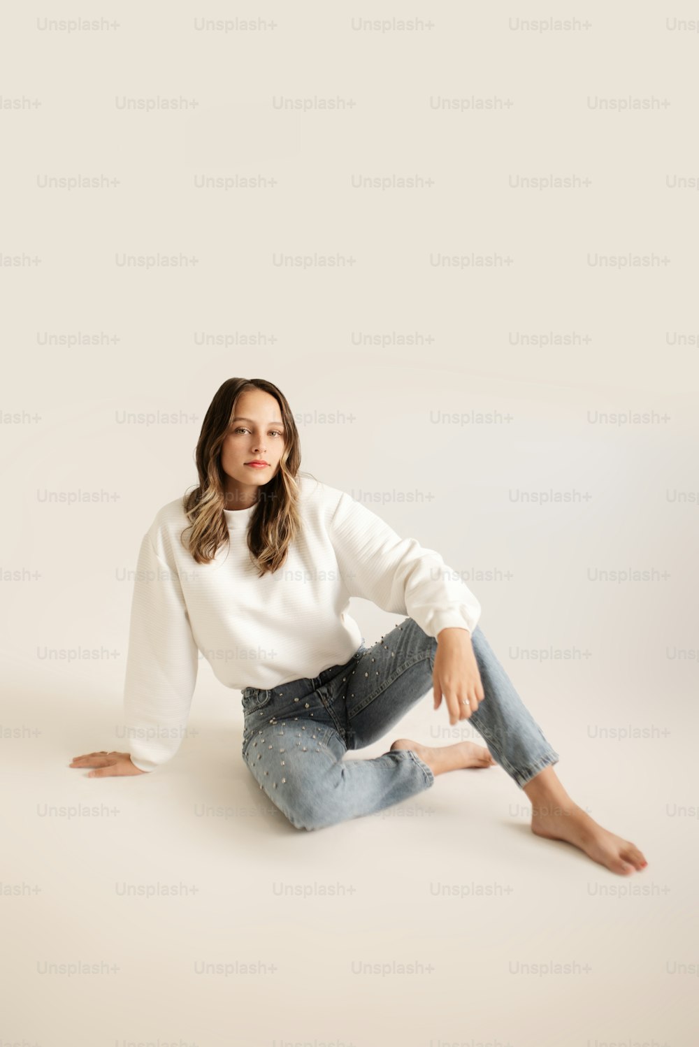 a woman sitting on the ground wearing jeans and a sweater