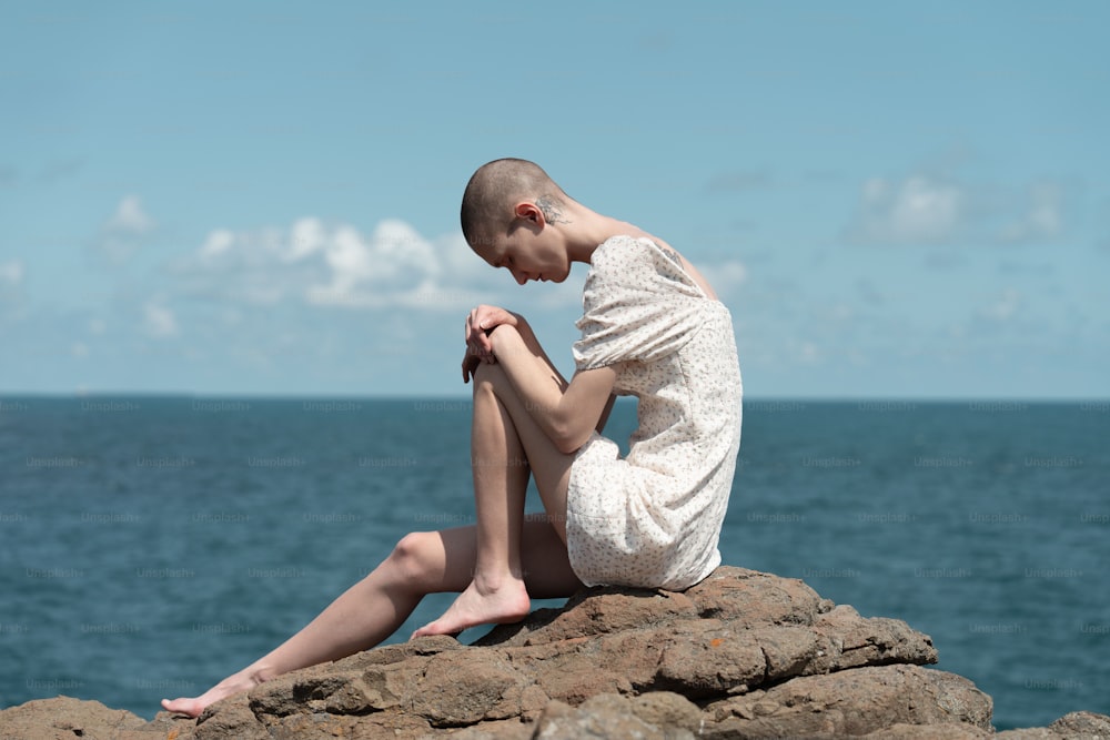 a woman sitting on a rock by the ocean