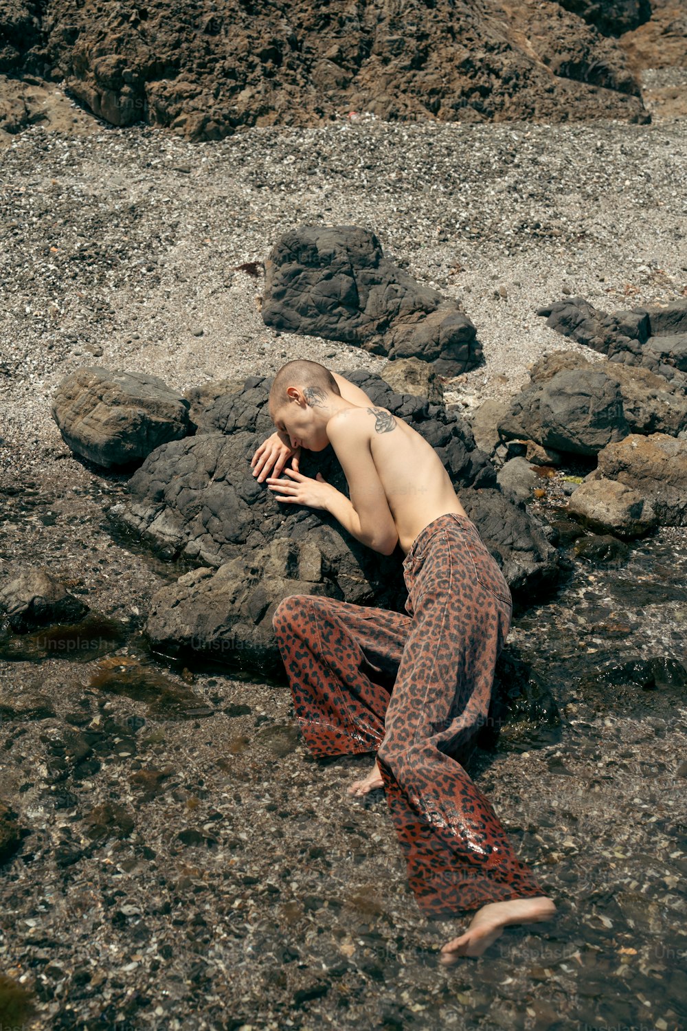 a man laying on a rocky beach next to a body of water