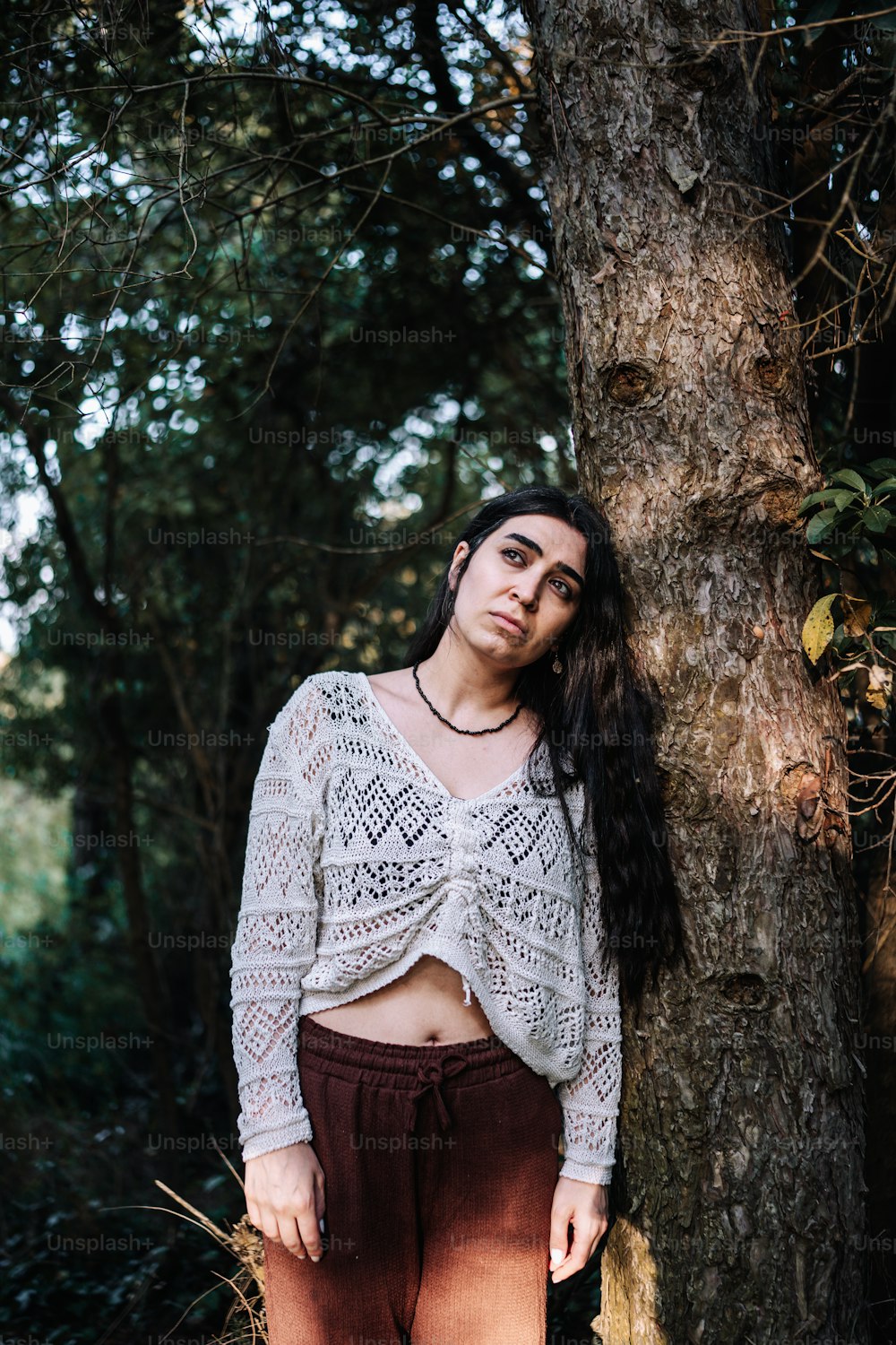 a woman standing next to a tree in a forest