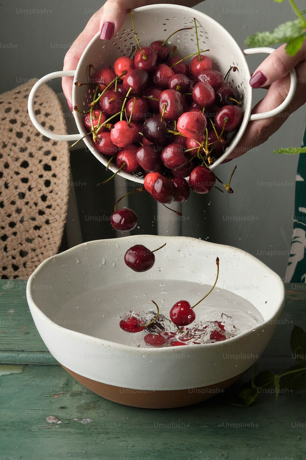 a person holding a bowl of cherries above a bowl of water