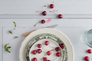 um prato branco coberto com cerejas ao lado de uma tigela de cerejas