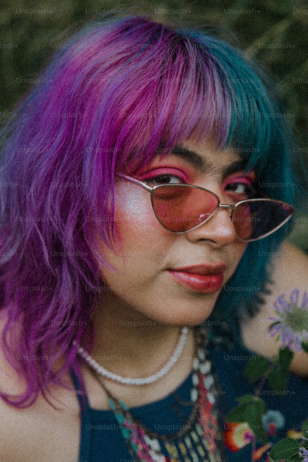 Eine Frau mit lila Haaren, die eine Brille und eine Halskette trägt