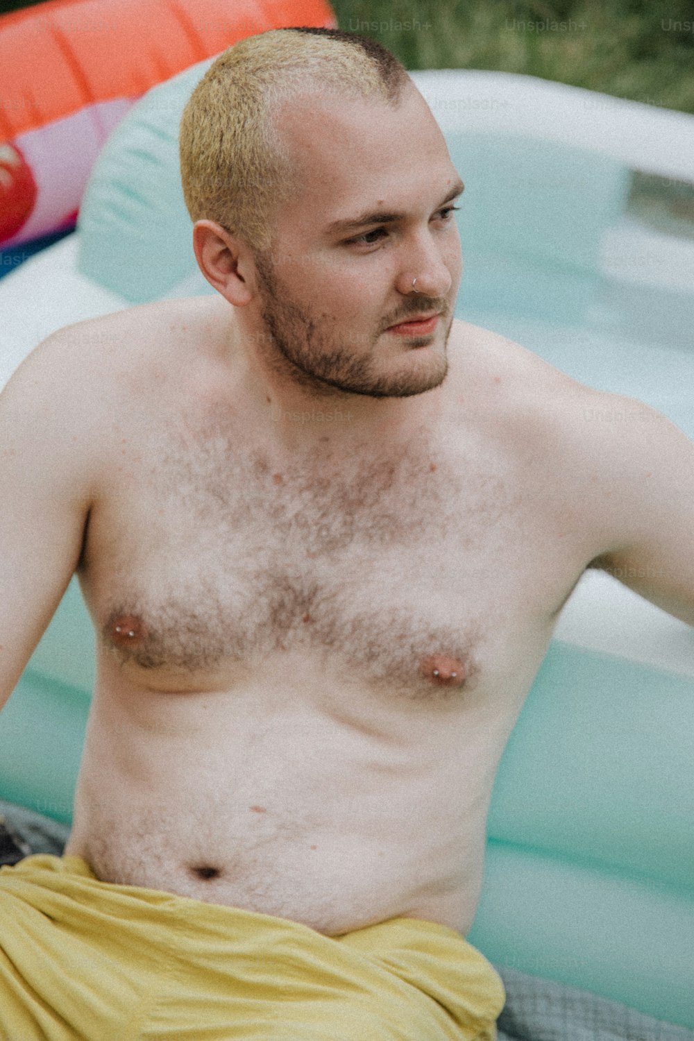 um homem sem camisa sentado em uma piscina com um frisbee