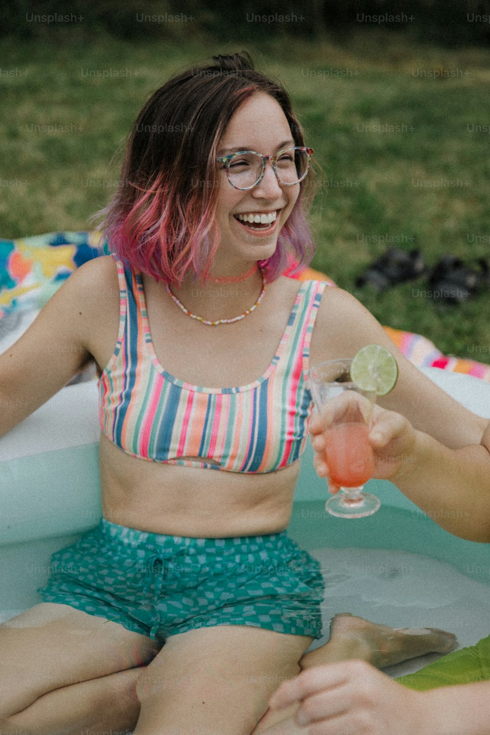 uma mulher em um top de biquíni segurando uma bebida em uma piscina