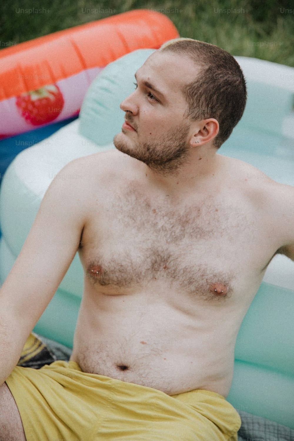 Un hombre sin camisa sentado junto a una piscina inflable