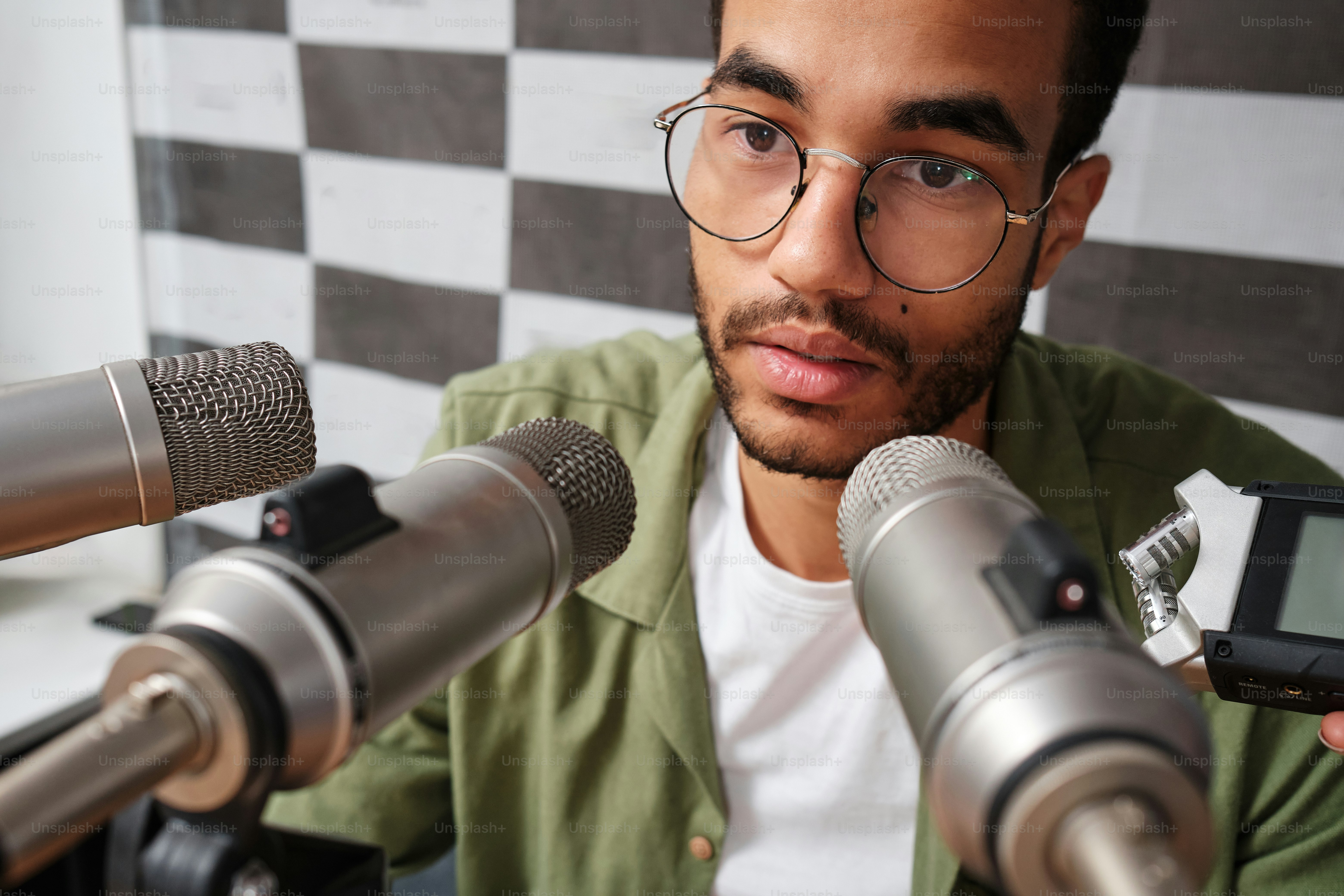 a man with glasses holding a cell phone in front of microphones