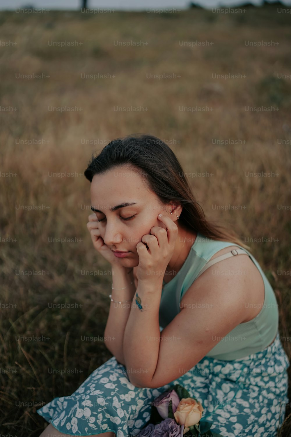 uma mulher sentada em um campo com as mãos no rosto
