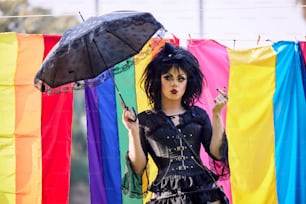 Una mujer sosteniendo un paraguas frente a una bandera del arco iris