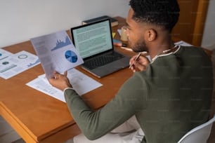 Ein Mann, der mit einem Laptop und Papieren an einem Schreibtisch sitzt