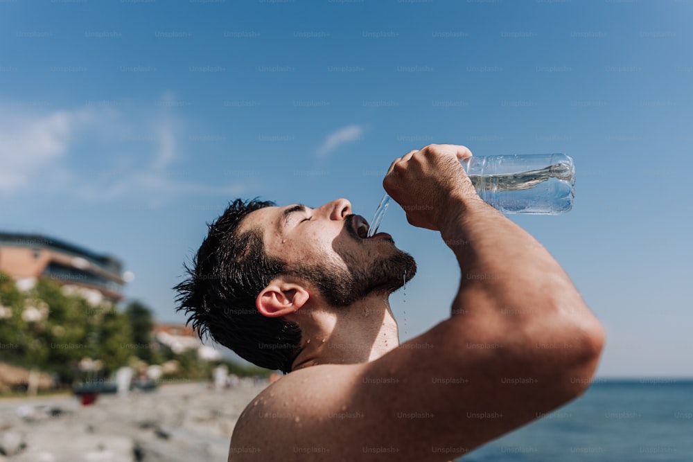 a man drinking water from a bottle on the beach