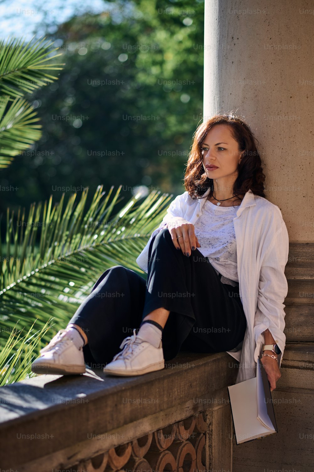 a woman sitting on a ledge next to a palm tree