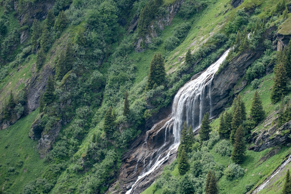 a waterfall in the middle of a lush green hillside