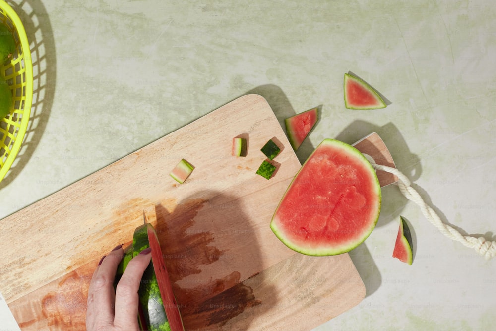 uma pessoa cortando um pedaço de melancia em uma tábua de corte