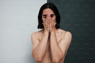 Um homem sem camisa cobre o rosto com as mãos