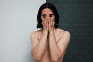 a shirtless man covers his face with his hands