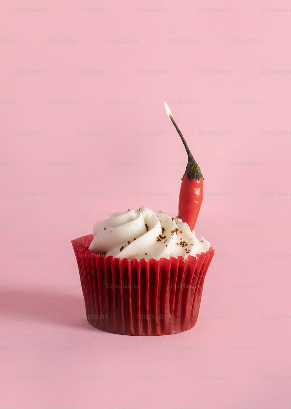 a cupcake with white frosting and a red pepper on top