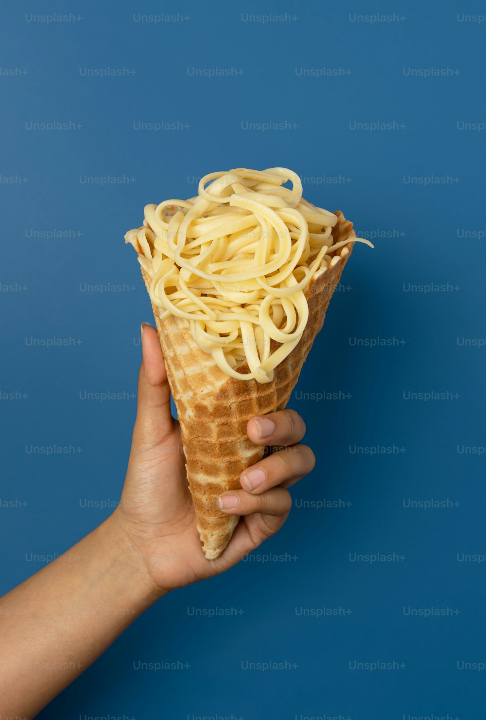 a hand holding an ice cream cone filled with noodles