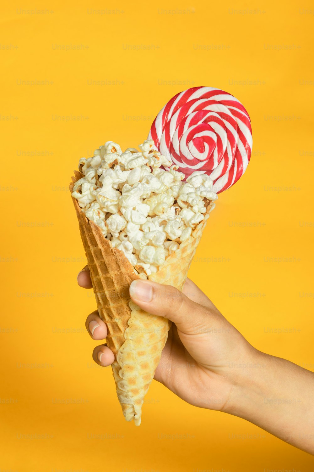 a hand holding a waffle cone filled with popcorn and a candy cane